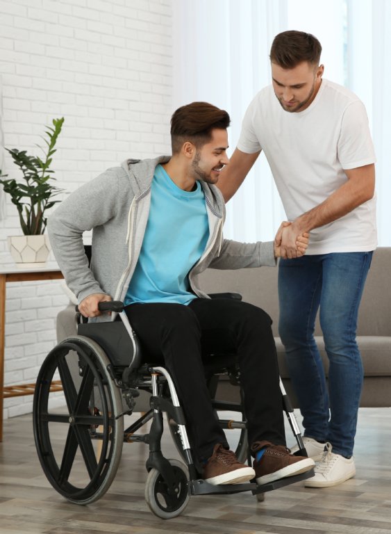 Pfleger hilft einem jungen Mann aus dem Rollstuhl